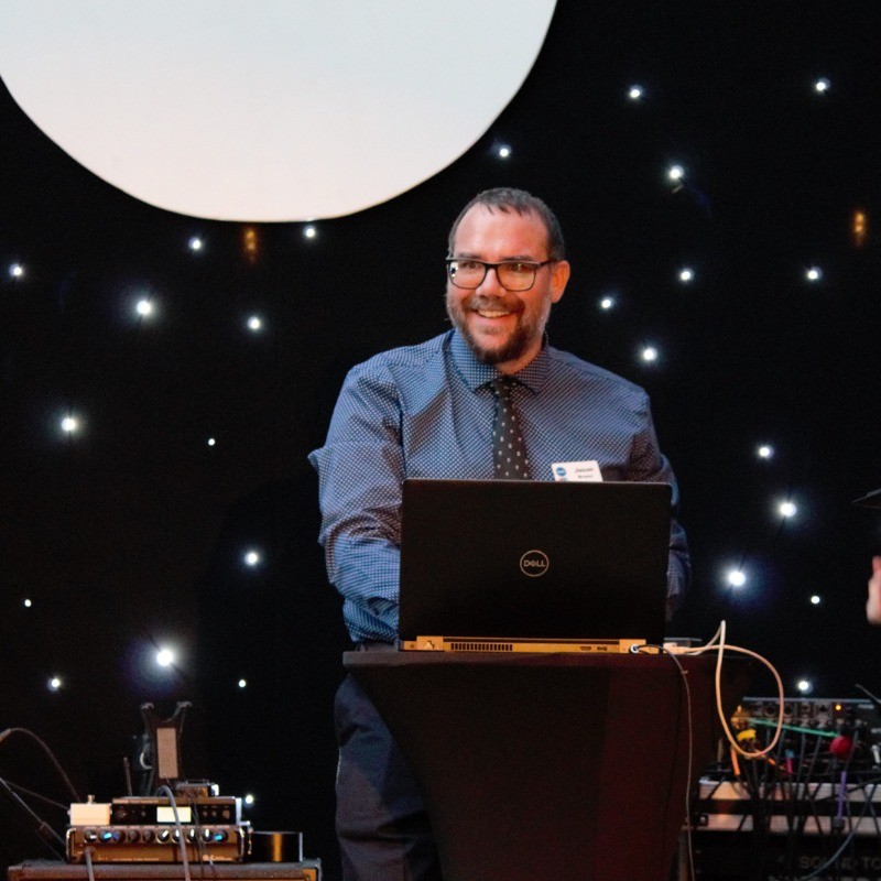 Jason Brown, on stage standing in front of a laptop. 